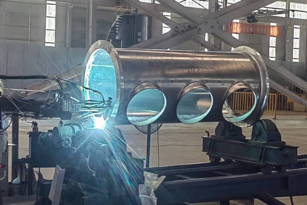 Automatic orbital welding of large heavy steel cylinder structure in industrial workshop.
